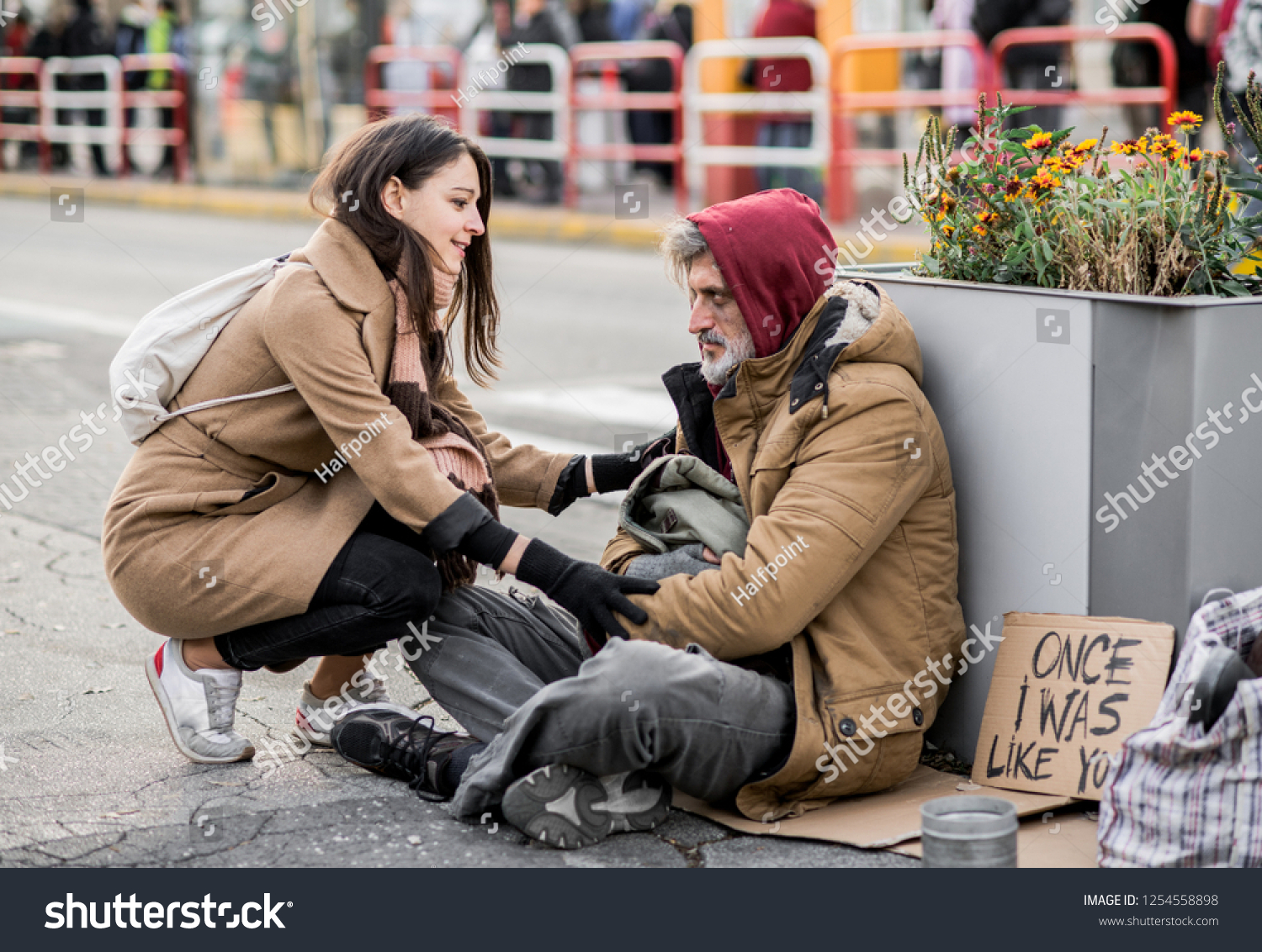 Young woman giving money to homeless beggar man sitting in city. #1254558898