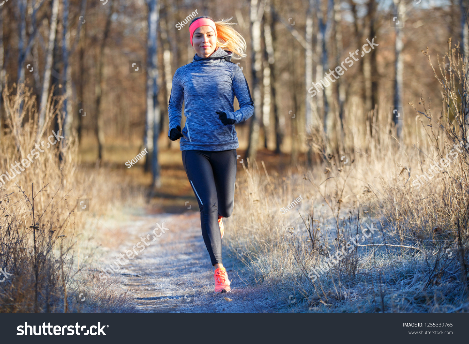 Young slim girl running in the park in early winter. Attractive woman jogging on snowy trail #1255339765