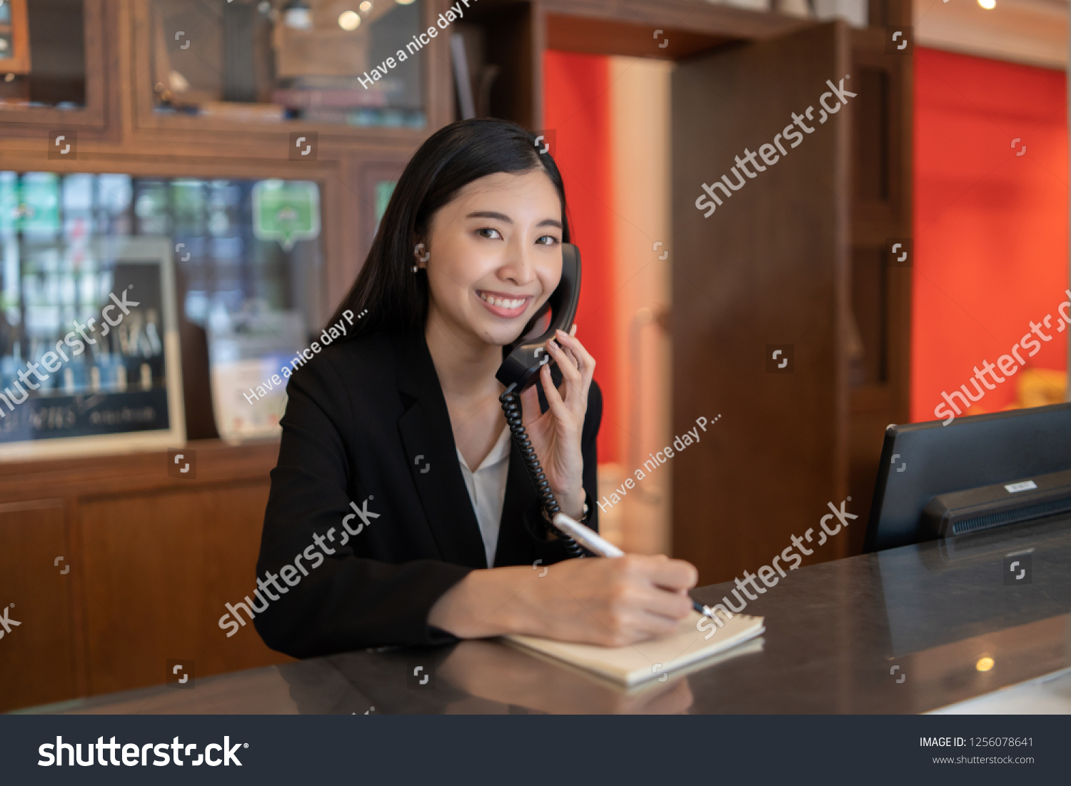 Welcome to the hotel,Happy young Asian woman hotel receptionist worker smiling standing,she taking  telephone call at a Modern luxury reception counter waiting for guests getting key card in hotel    #1256078641