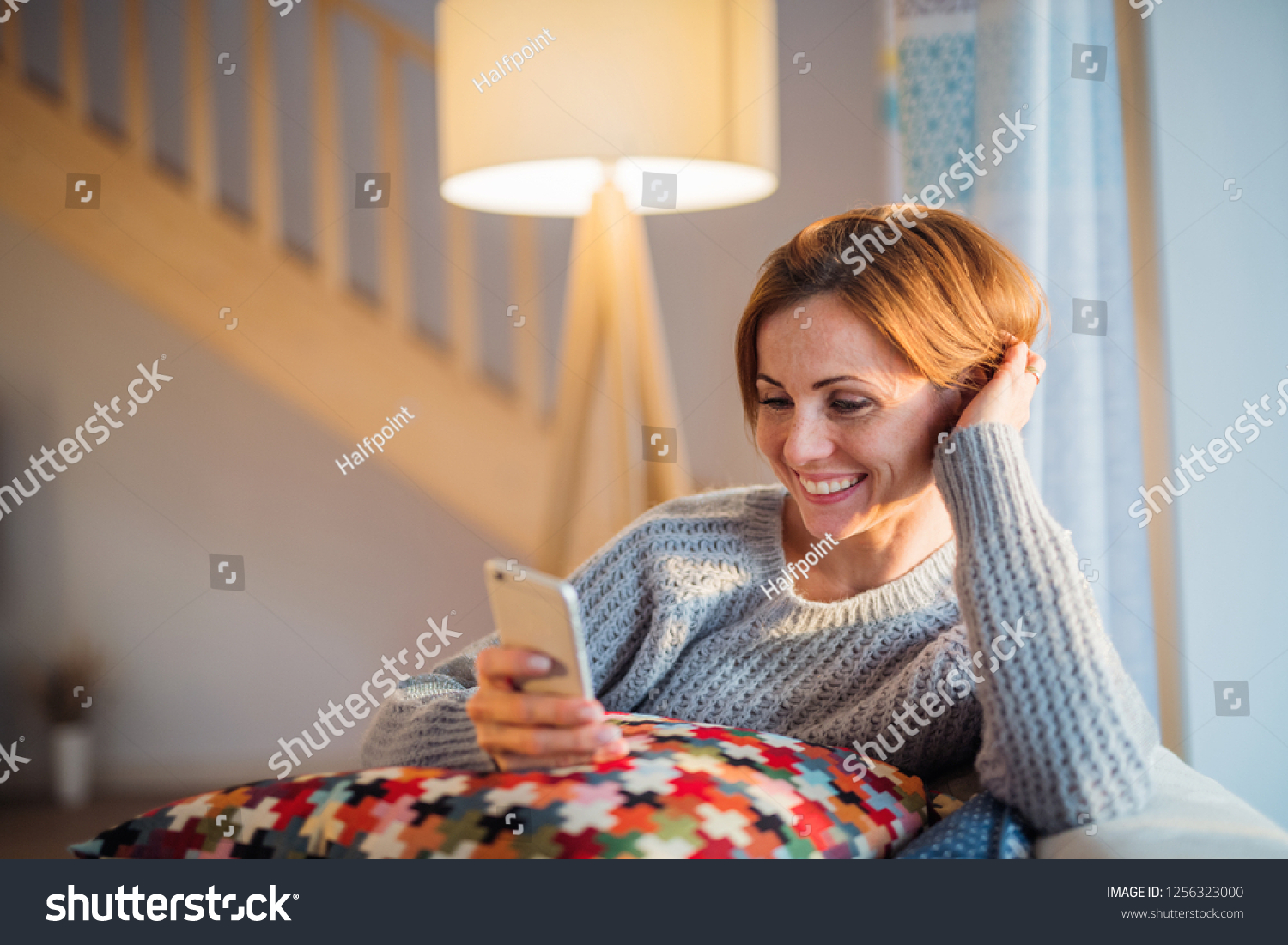 A young woman sitting indoors on a sofa at home, using smartphone. #1256323000