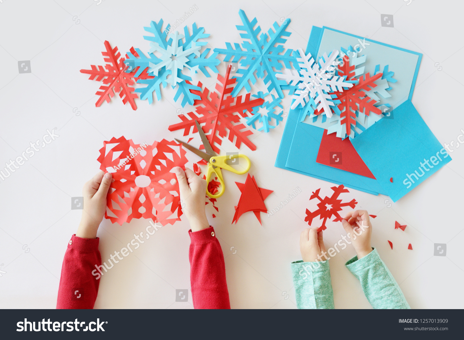 top view. Children's hands cut out on a white background blue and red snowflakes from paper #1257013909