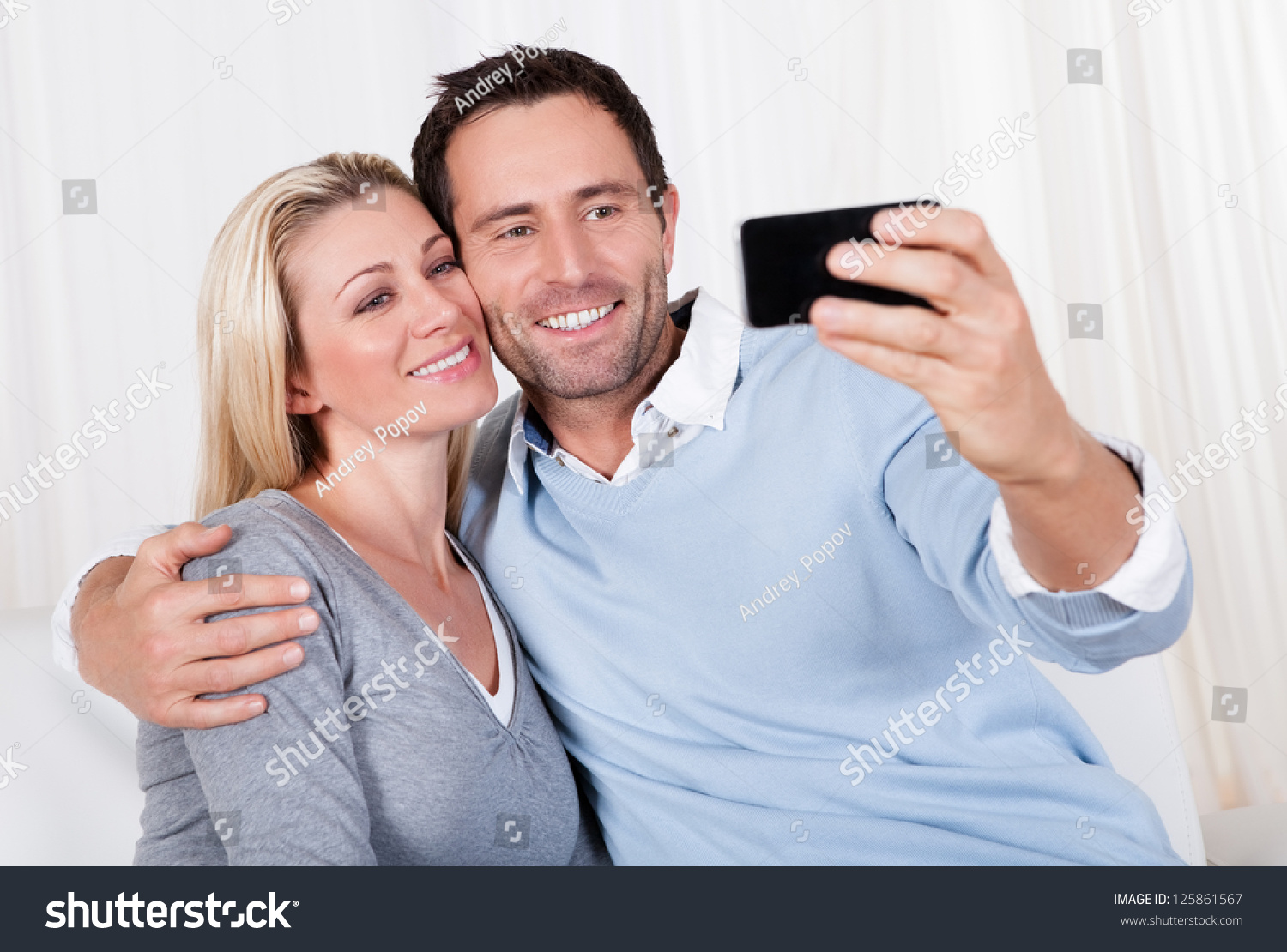 Beautiful smiling young couple photographing themselves on a mobile or smartphone posing close together with his arm around her #125861567