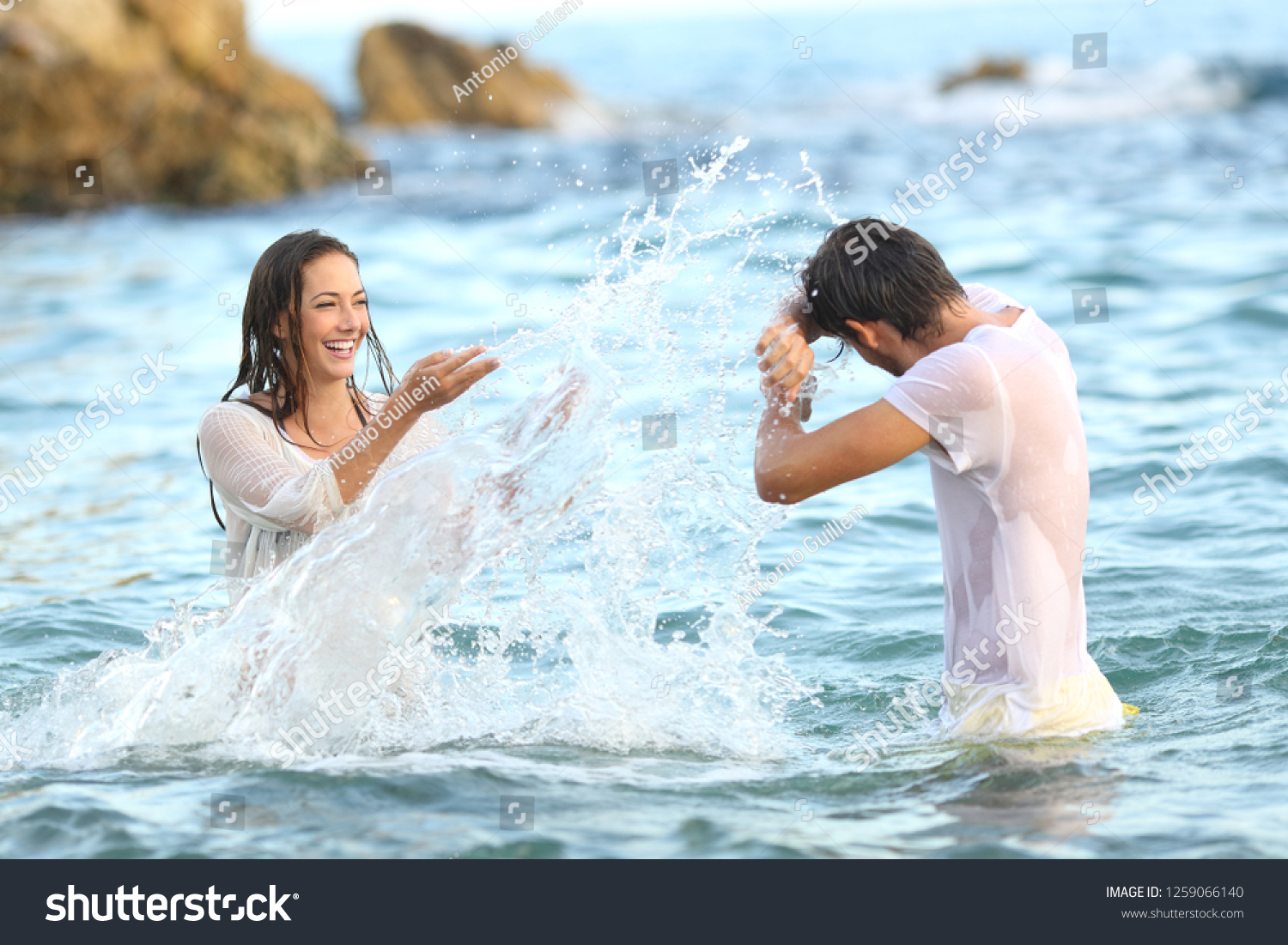 Spontaneous couple joking throwing water bathing in the sea on the beach #1259066140