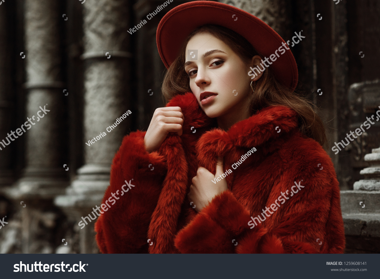 Outdoor close up fashion portrait of young beautiful confident woman wearing trendy orange faux fur coat, hat, silvery hoop earrings, posing in street of european city. Copy, empty space for text
 #1259608141