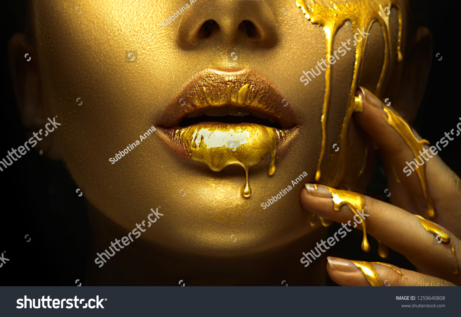 Gold Paint smudges drips from the face lips and hand, lipgloss dripping from sexy lips, golden liquid drops on beautiful model girl's mouth, gold metallic skin make-up. Beauty woman makeup close up. #1259640808