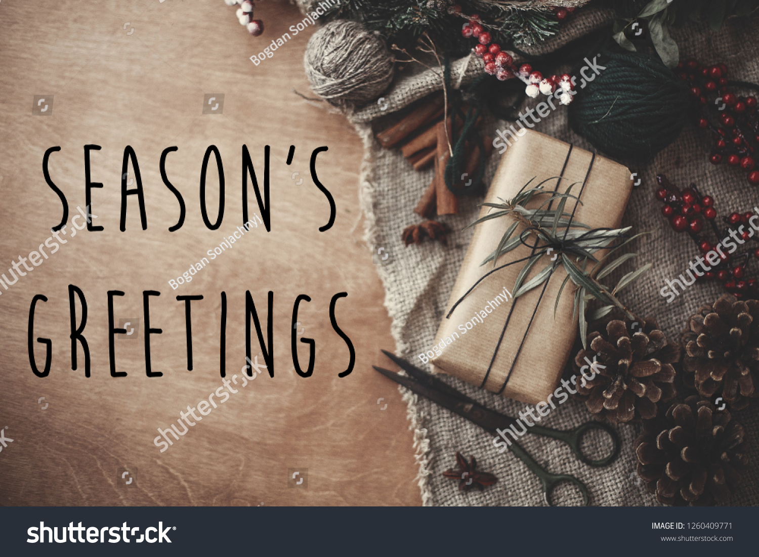 Season's greetings text sign on stylish rustic christmas gift box with fir branches, red berries, pine cones, cinnamon on rustic wood. Atmospheric image. Seasonal greeting card #1260409771