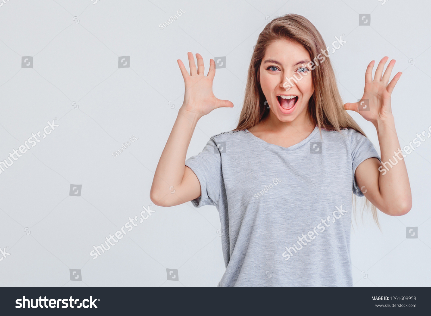 Surprised joyful girl on gray background in t-shirt looks with smile and holds hands with palm open at head. Concept of surprise solemnity surprise. Copy space left. Closeup. #1261608958