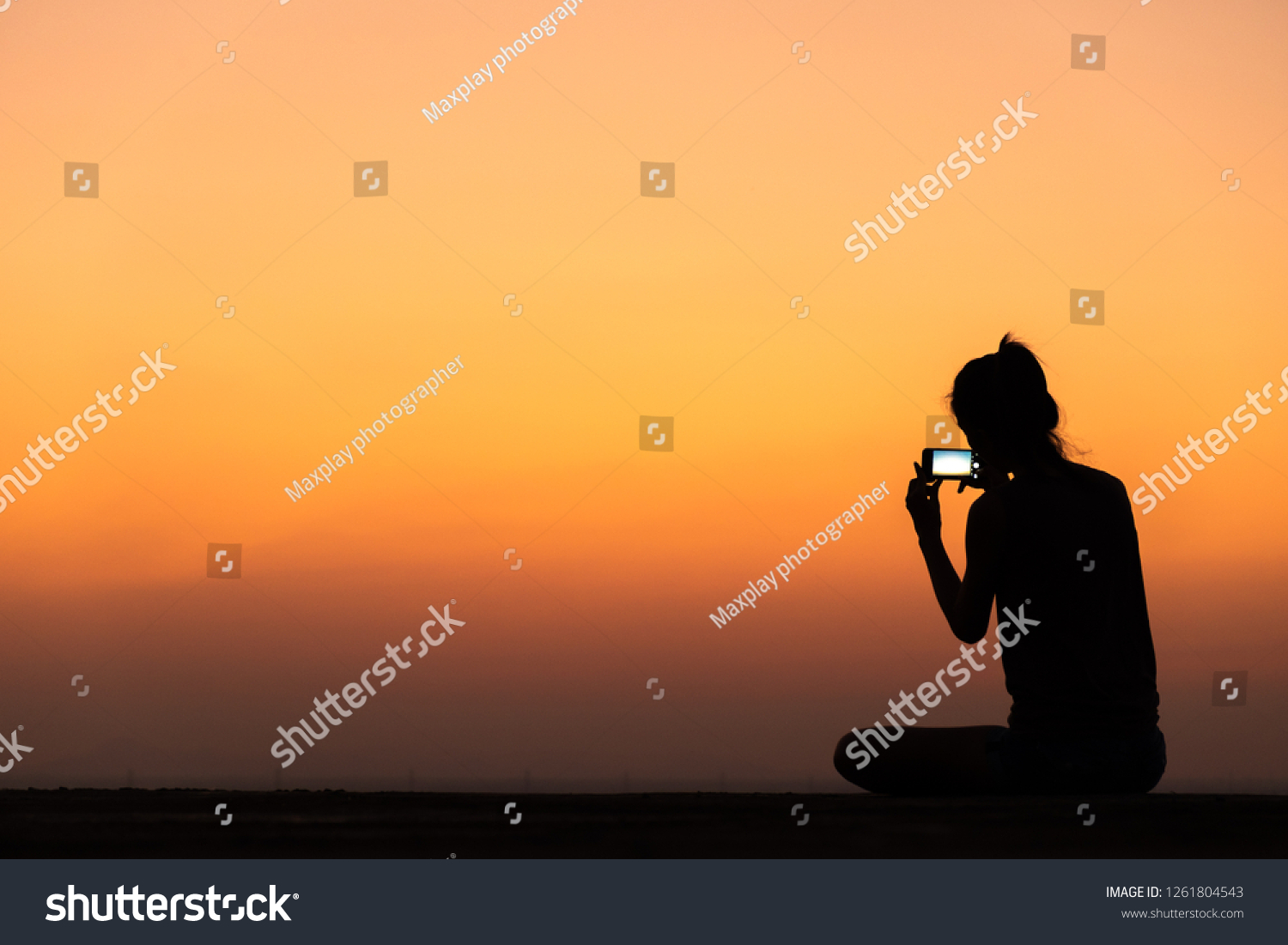 silhouette of young woman taking photo with smartphone at sunset #1261804543