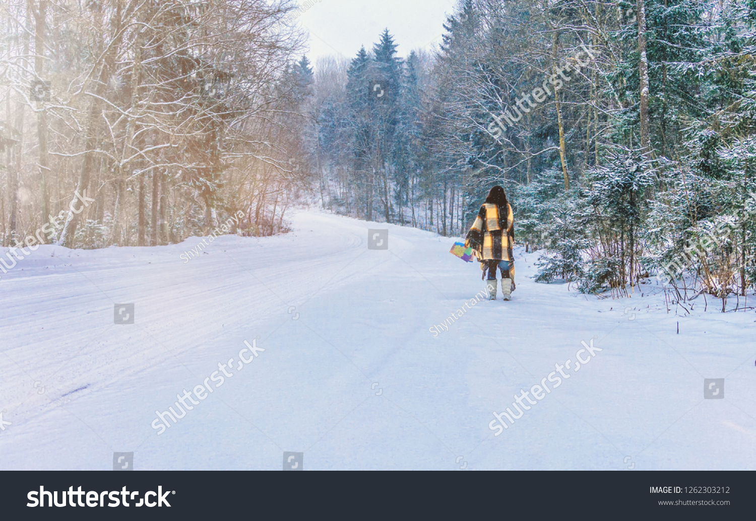 Beautiful woman standing among snowy trees in winter forest and enjoying first snow. Wearing hat, plaid scarf and coat. Wanderlust and boho style #1262303212