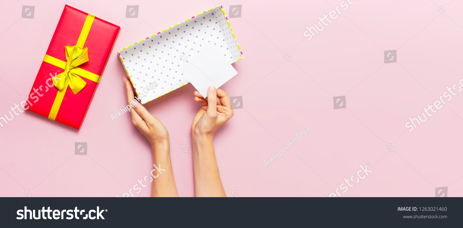 Woman hands holding present red box with gold ribbon on pink background Flat lay top view. Present for birthday, surprise, valentine day, Christmas, New Year. Congratulations background copy space. #1263021460