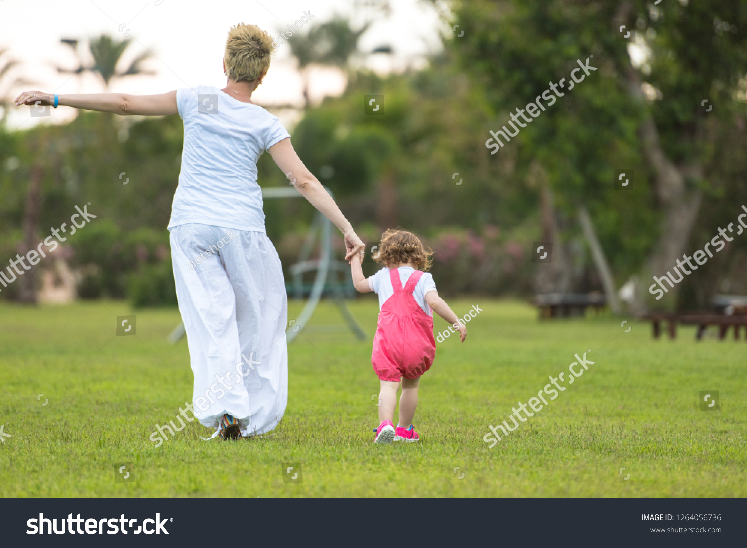 Young Mother and cute little daughter enjoying free time playing outside at backyard on the grass, happy family in nature concept #1264056736