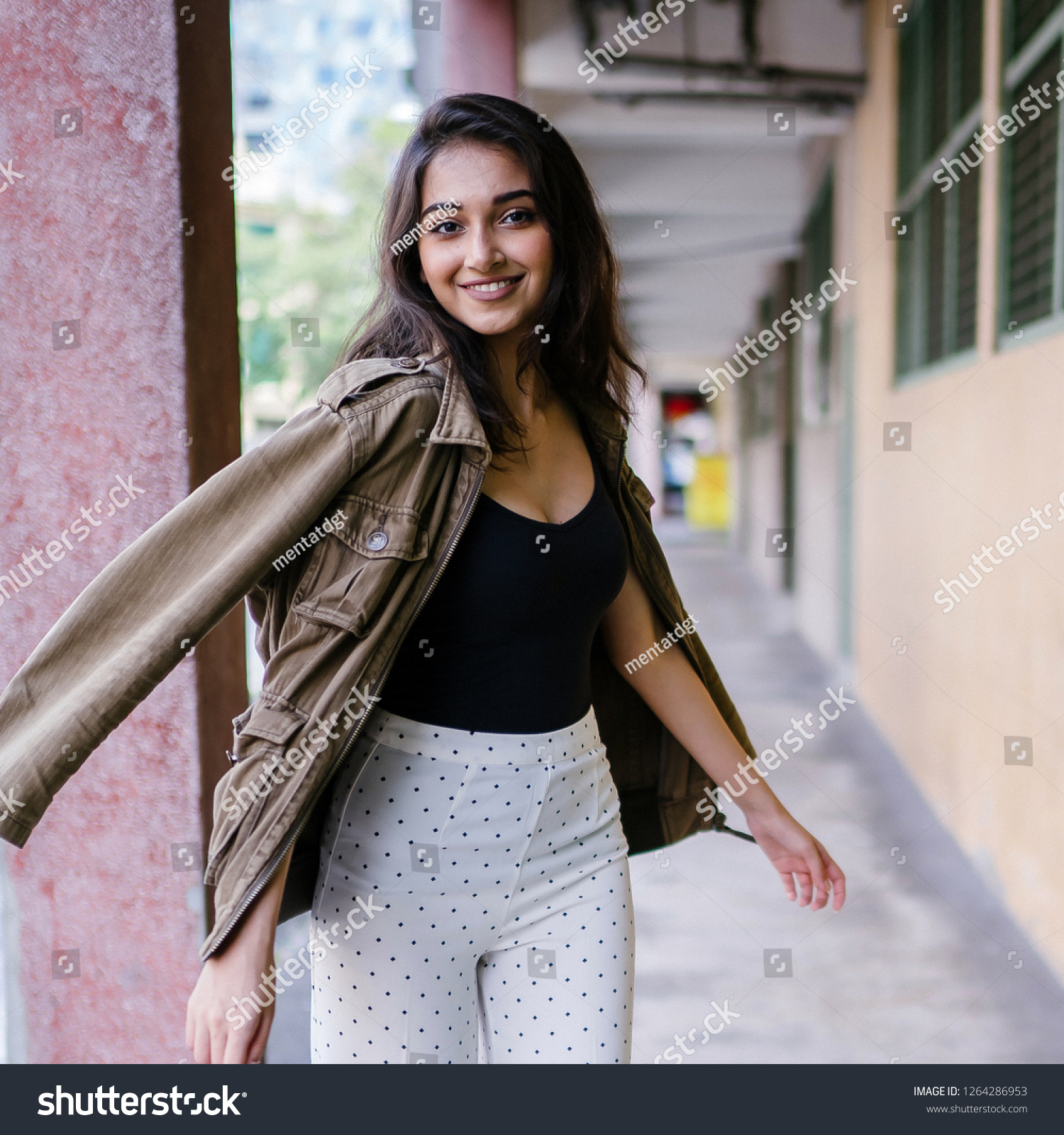 A beautiful, stylish, tall and elegant Indian Asian woman walks down a corridor and spins around to smile at the camera. She is beautiful and confident.  #1264286953