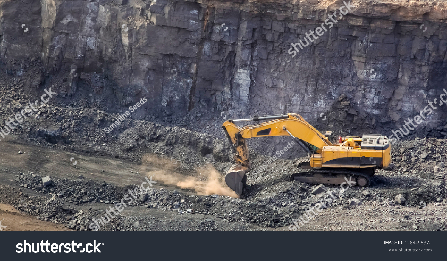 Yellow excavator digging for ore rich rock in an open pit mine #1264495372