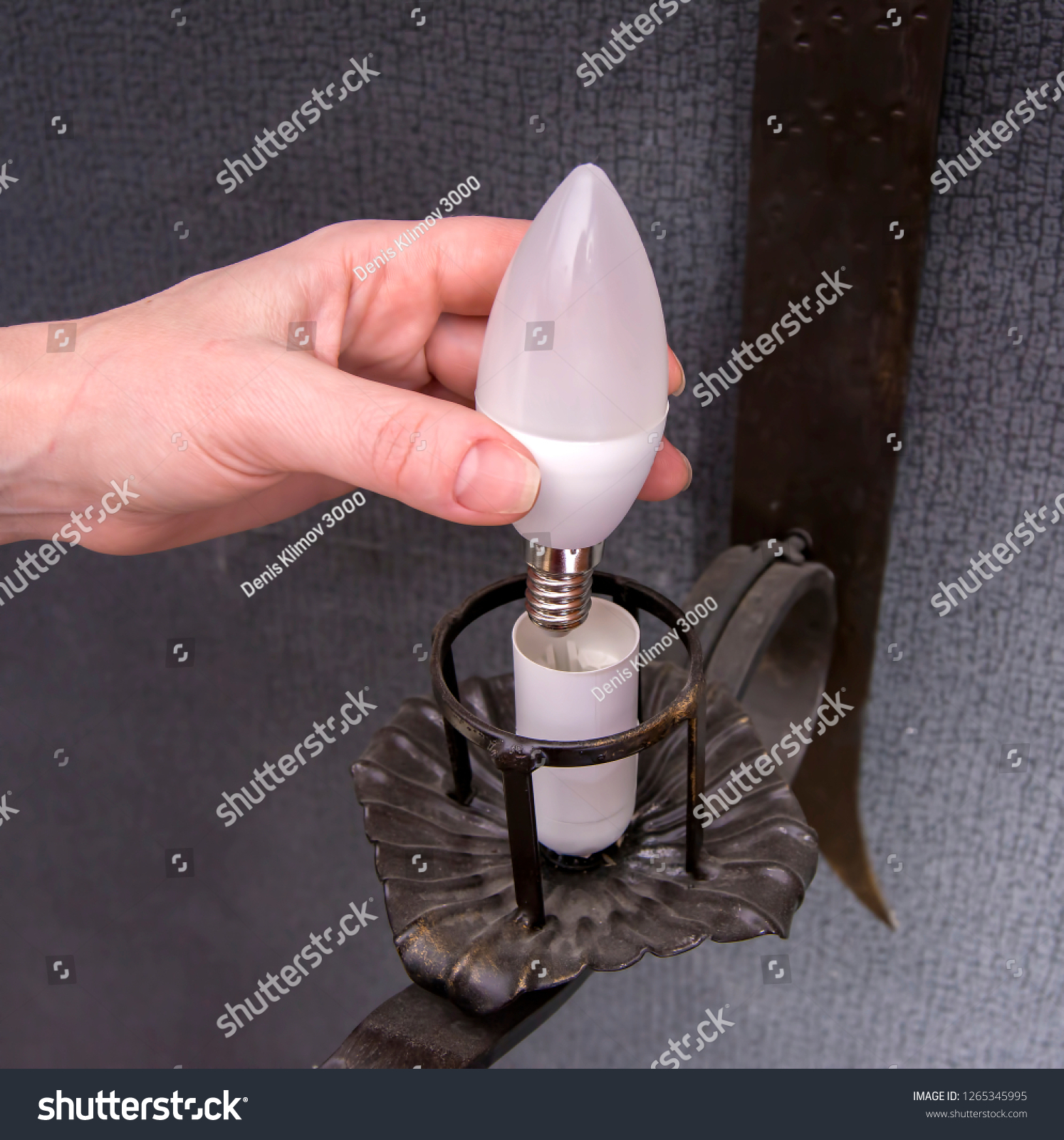 A woman's hand inserts an led light bulb into the wall lamp. #1265345995