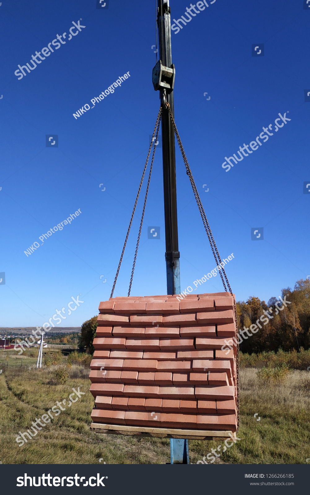 The car crane holds and unloads the brick on the background of the blue autumn sky #1266266185