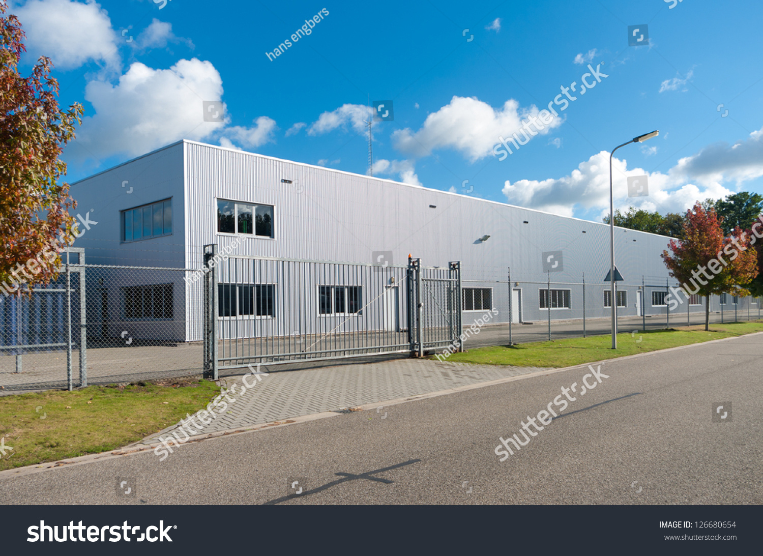 modern exterior of an industrial building, surrounded by a fence with iron gate #126680654