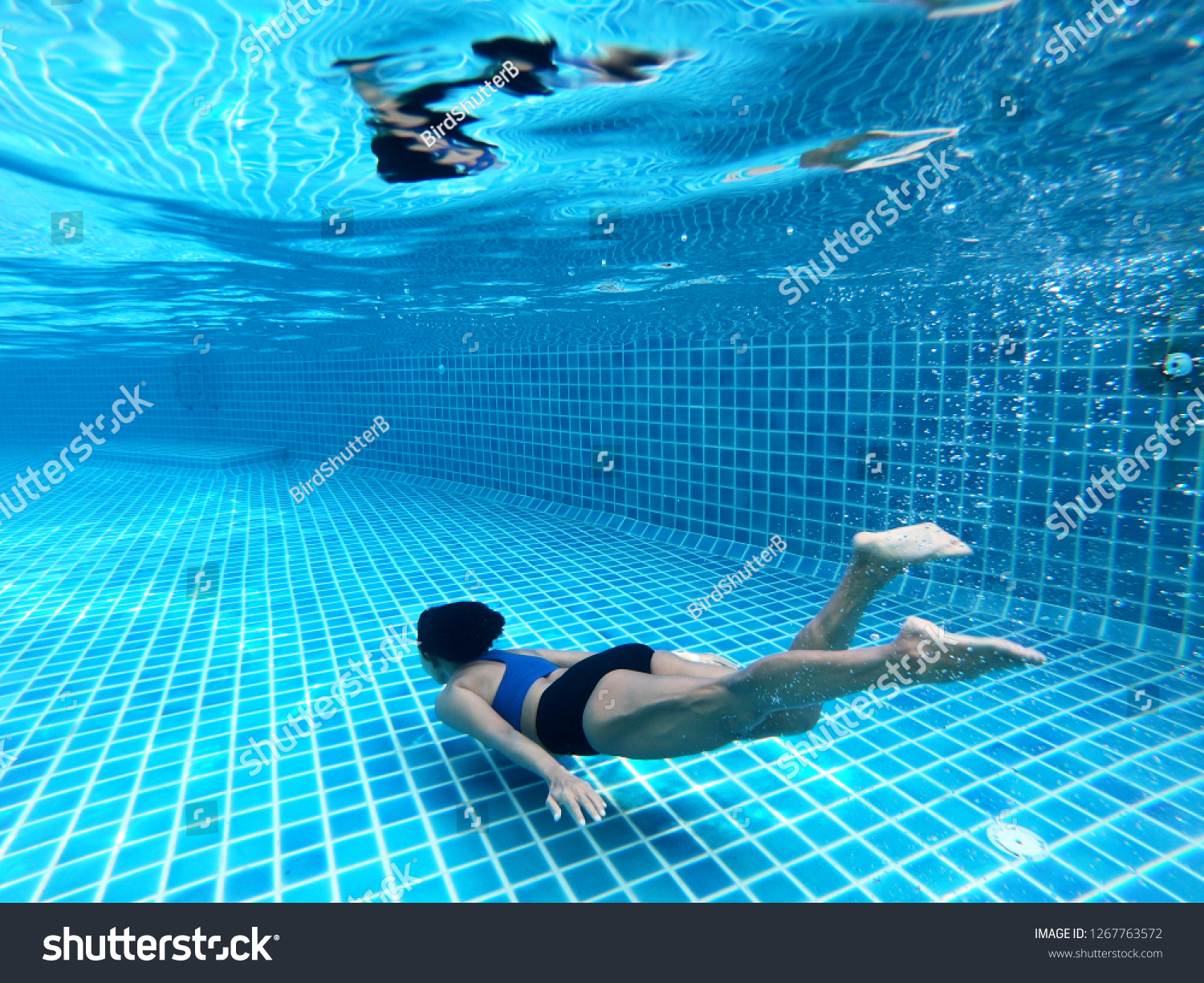 Woman swimming underwater or diving in the swimming pool, as background. Summer or sports concept. #1267763572
