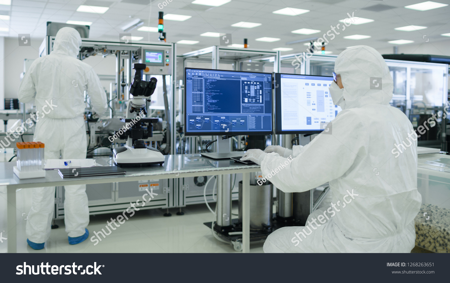 Shot of a Scientists in Sterile Suits Working with Computers, Analyzing Data form Modern Industrial Machinery in the Laboratory. Product Manufacturing Process: Pharmaceutics, Semiconductors #1268263651