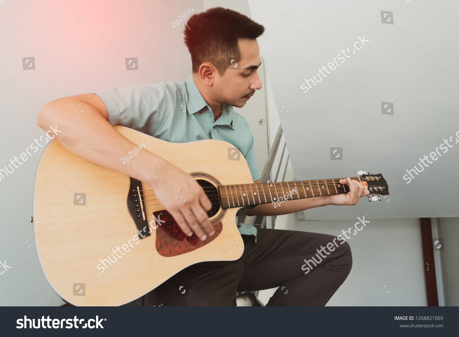 Cheerful guitarist. Cheerful handsome young man playing guitar and smiling while sitting on banister, Vintage color #1268821069