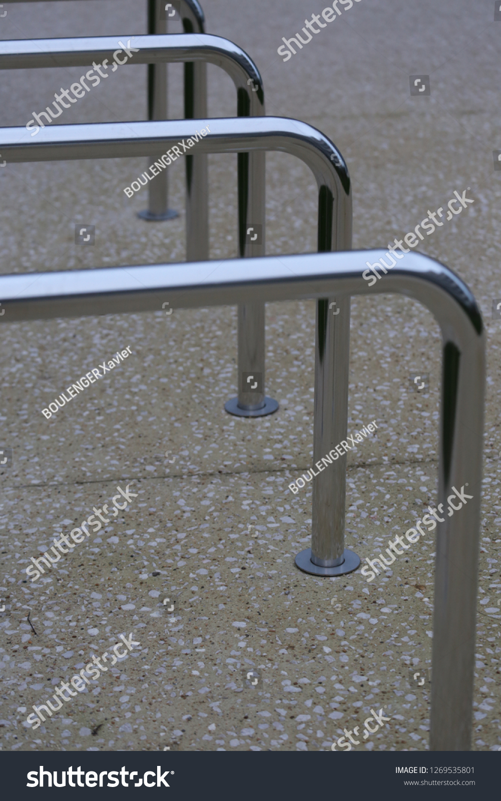 Close up view of pattern of curved inox tubes used to place bikes in a french city. Abstract urban image with curving lines. Metallic lighted objects with vertical and horizontal shapes.   #1269535801