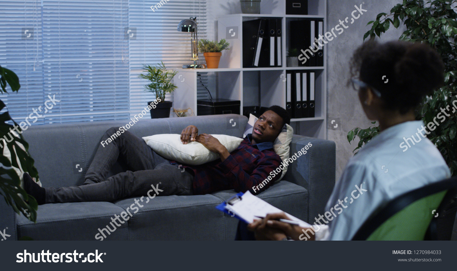 Medium shot of young man lying on a couch while talking to a psychologist #1270984033