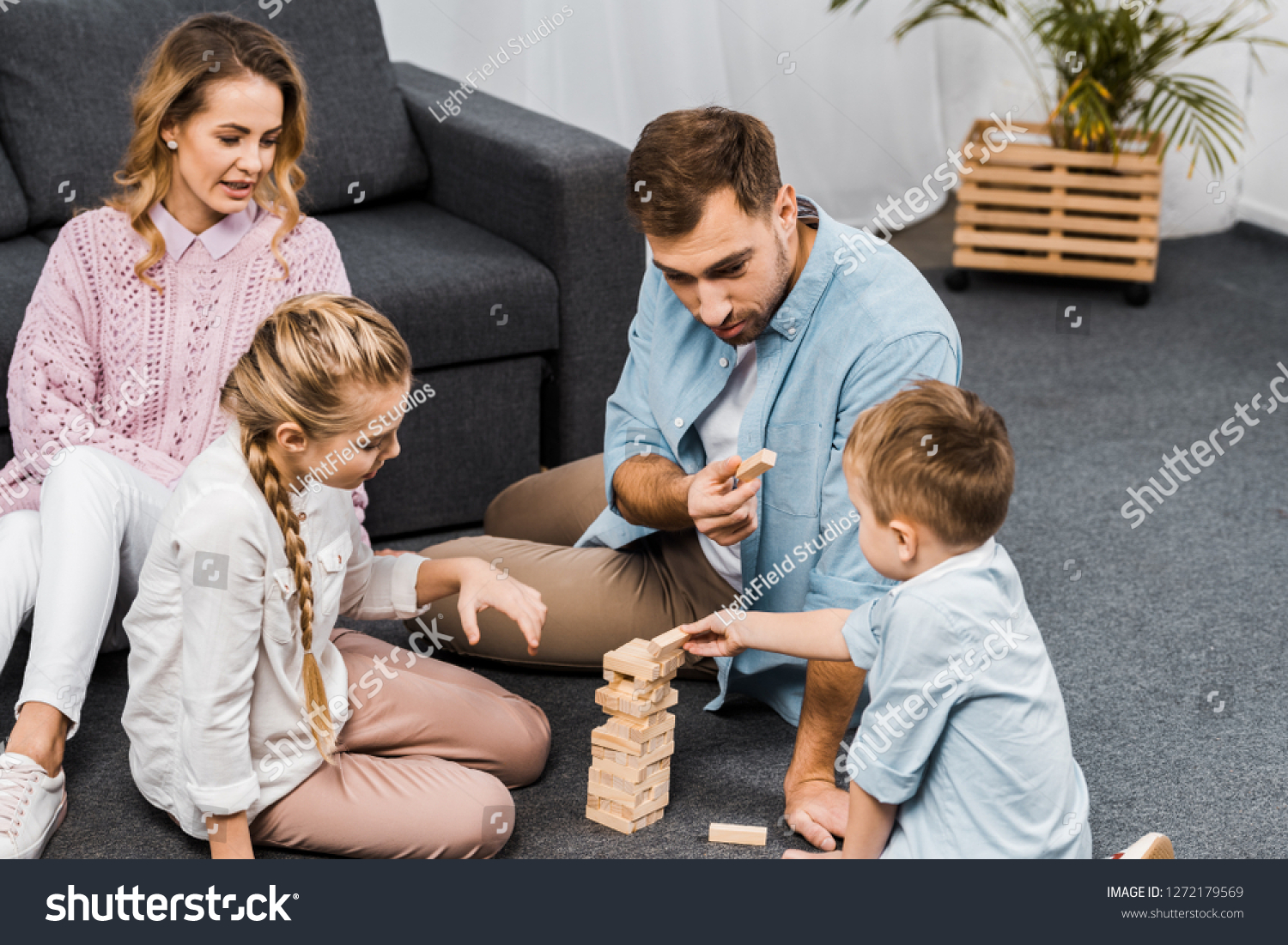 two parents playing blocks wood tower game with children on floor in apartment #1272179569