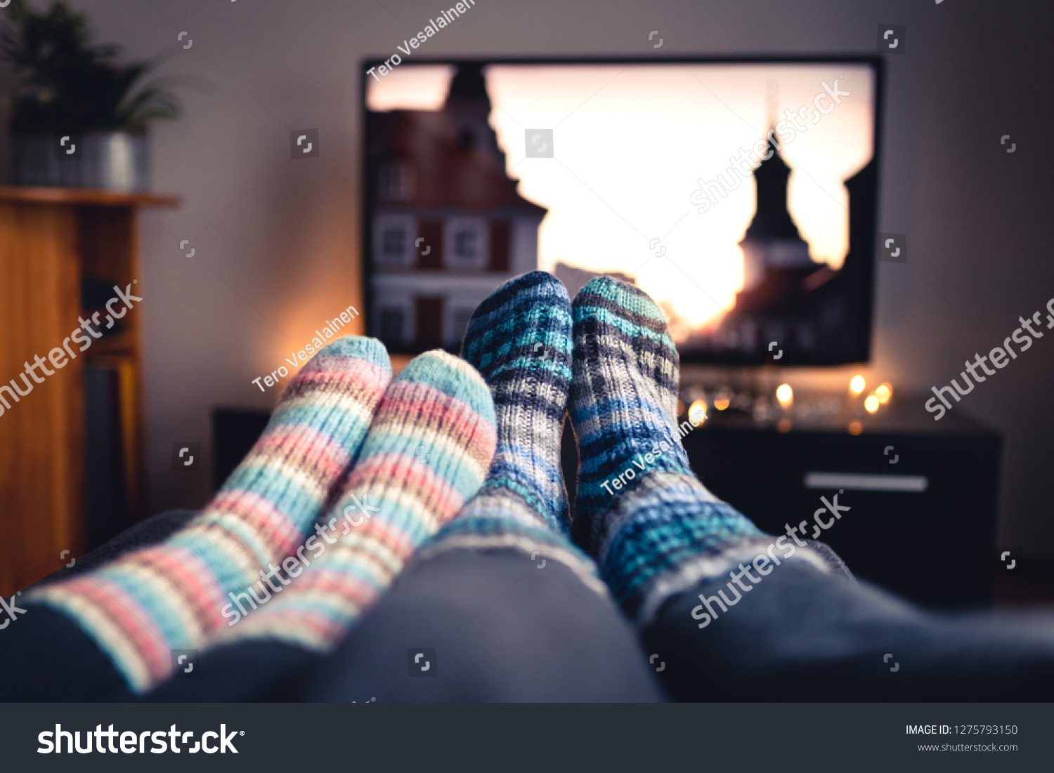 Couple with socks and woolen stockings watching movies or series on tv in winter. Woman and man sitting or lying together on sofa couch in home living room using online streaming service in television #1275793150