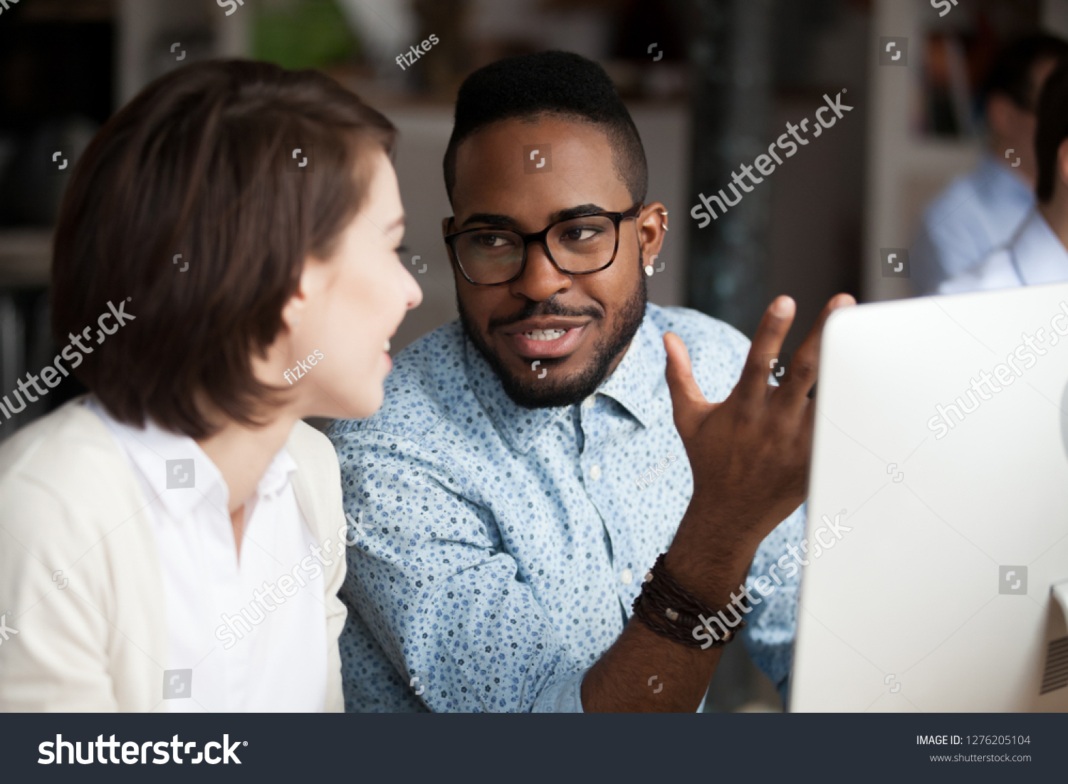 Friendly diverse colleagues having conversation in office, creative african american and caucasian workers discussing work chatting, black male worker talking to female coworker collaboration concept #1276205104