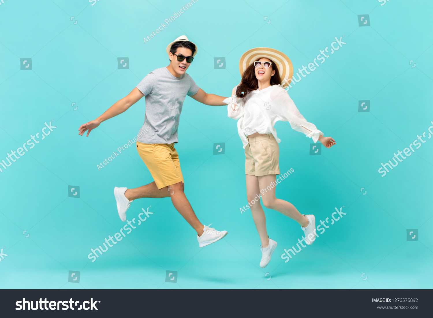 Playful energetic Asian couple in summer beach casual clothes jumping isolated on light blue background studio shot #1276575892