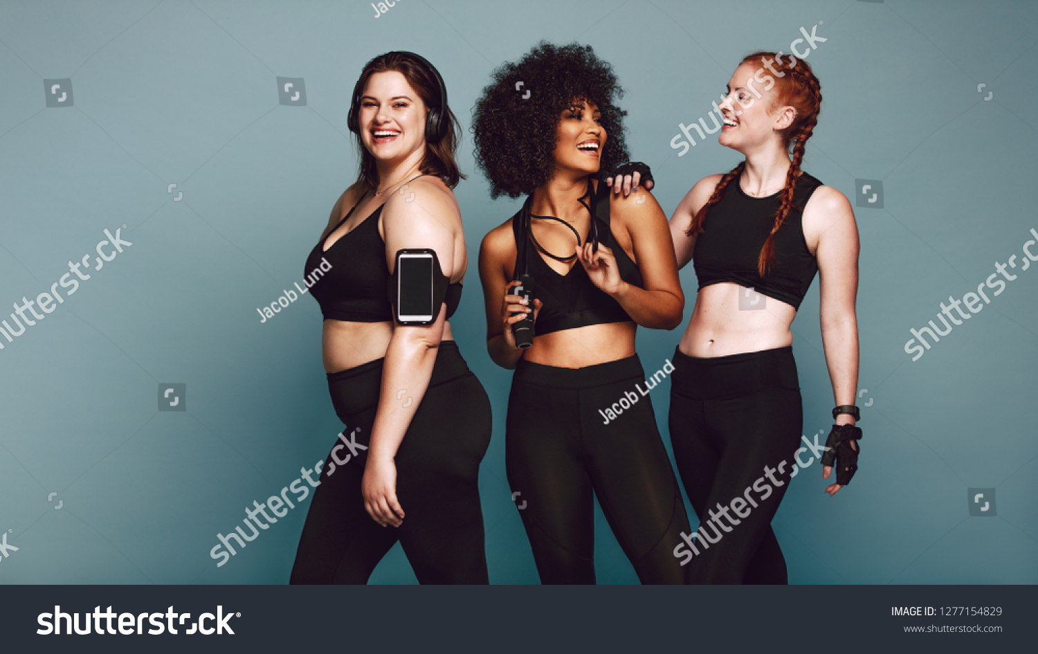 Multi-ethnic group of women together against grey background and smiling. Diverse group females in sportswear after workout. #1277154829