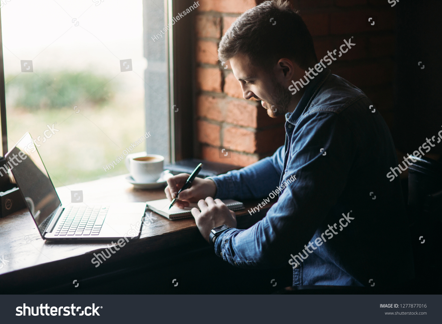 Man with a beard uses a laptop in a cafe and writes a note #1277877016