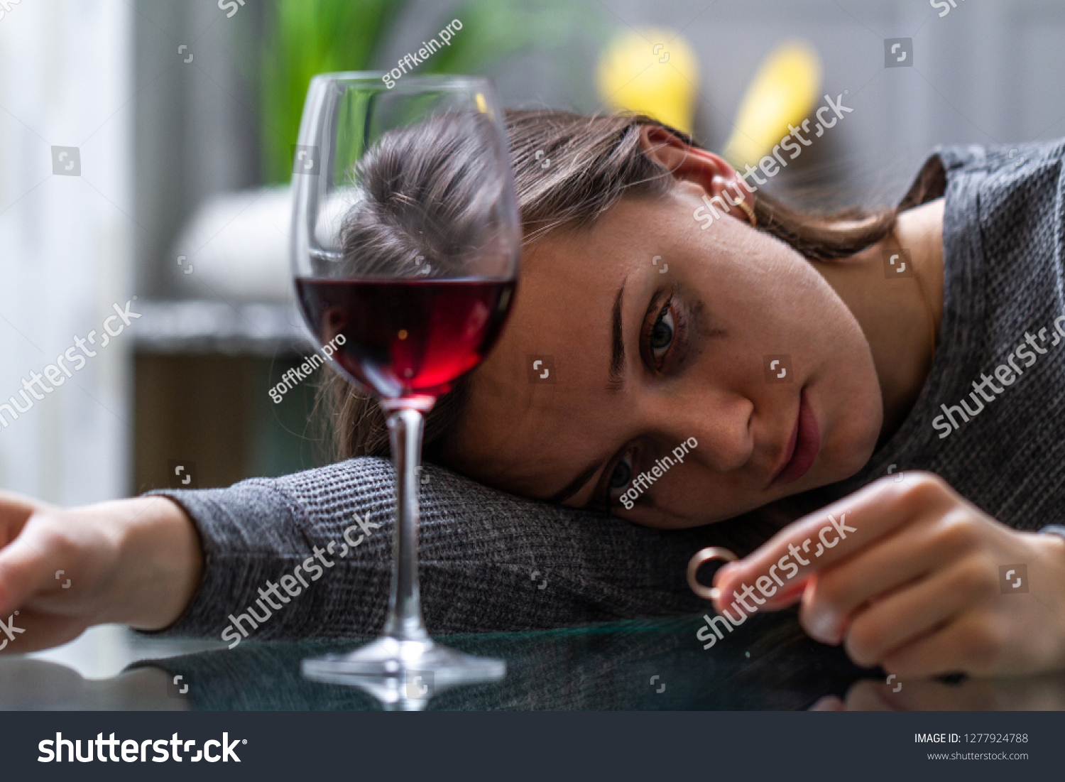 Crying, divorced woman holding a wedding ring and drinking alone red wine because of adultery, the betrayal of her husband and a failed marriage. Divorce concept. #1277924788