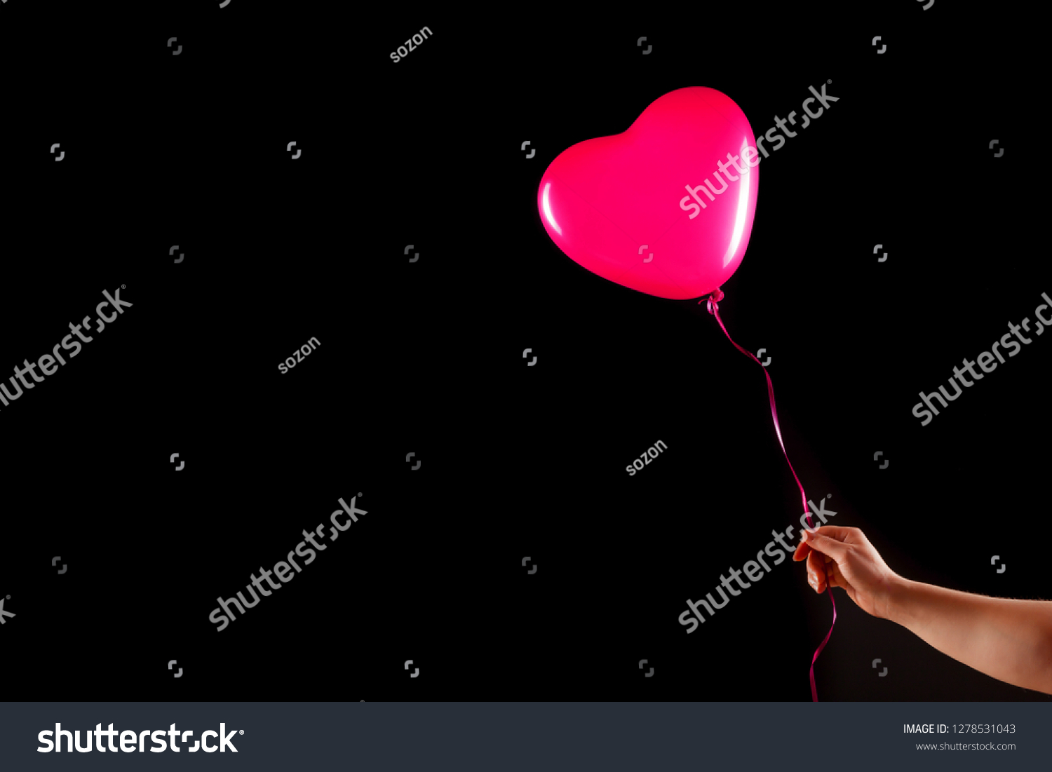 Female hand holds red rubber inflatable heart shape balloon. Love, relationship, valentines day and birthday celebration concept. Studio shot on an abstract blurred background with blank copy space #1278531043