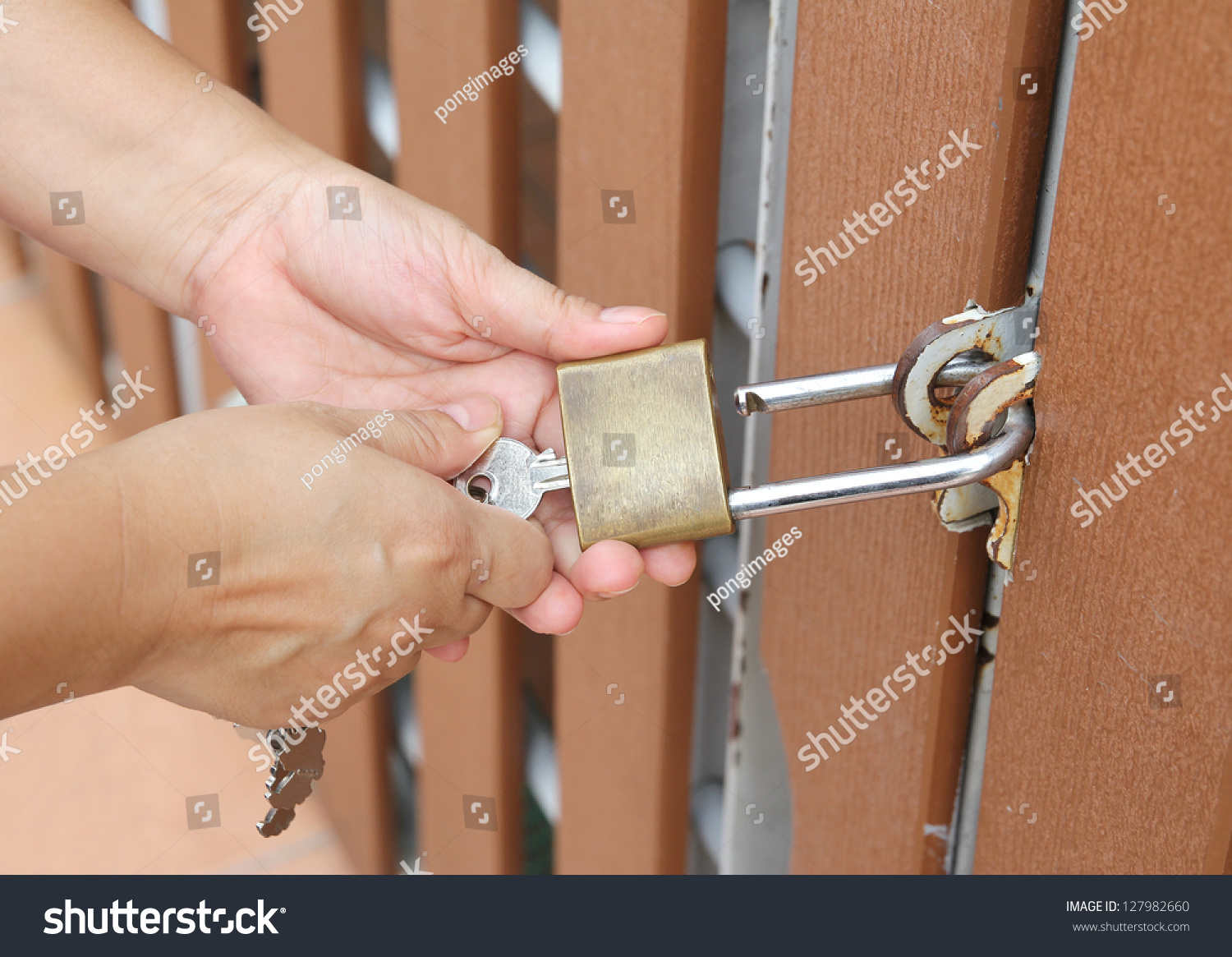 Closeup image of hand use key to open padlock and the brown wooden door #127982660