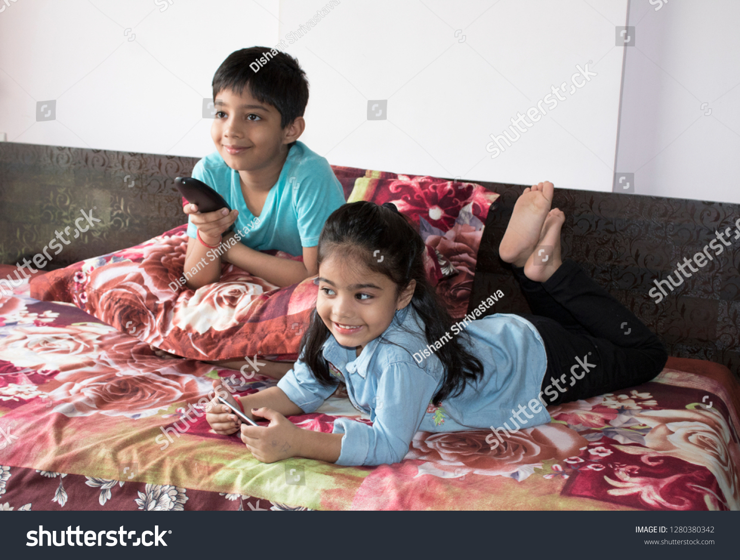 Girl using mobile phone while brother is watching tv on bed #1280380342