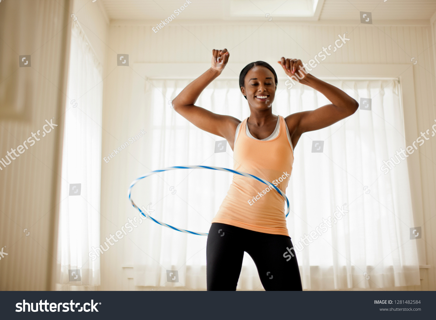Happy young woman hula hooping in her living room. #1281482584