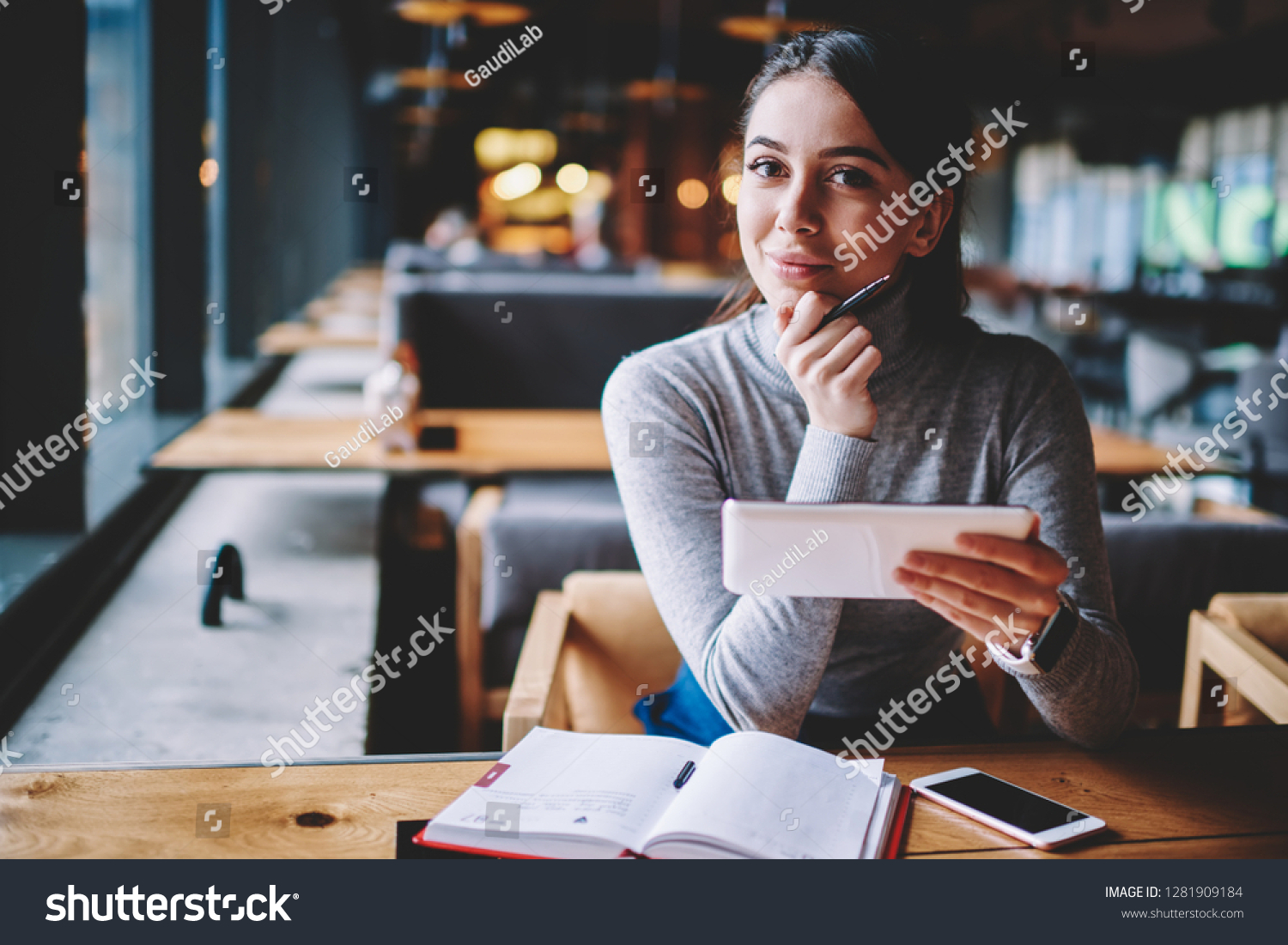 Portrait of beautiful young smiling blogger looking in camera while enjoying break at cafe and creating new publication for own website, happy hipster girl holding electronic device and chatting #1281909184
