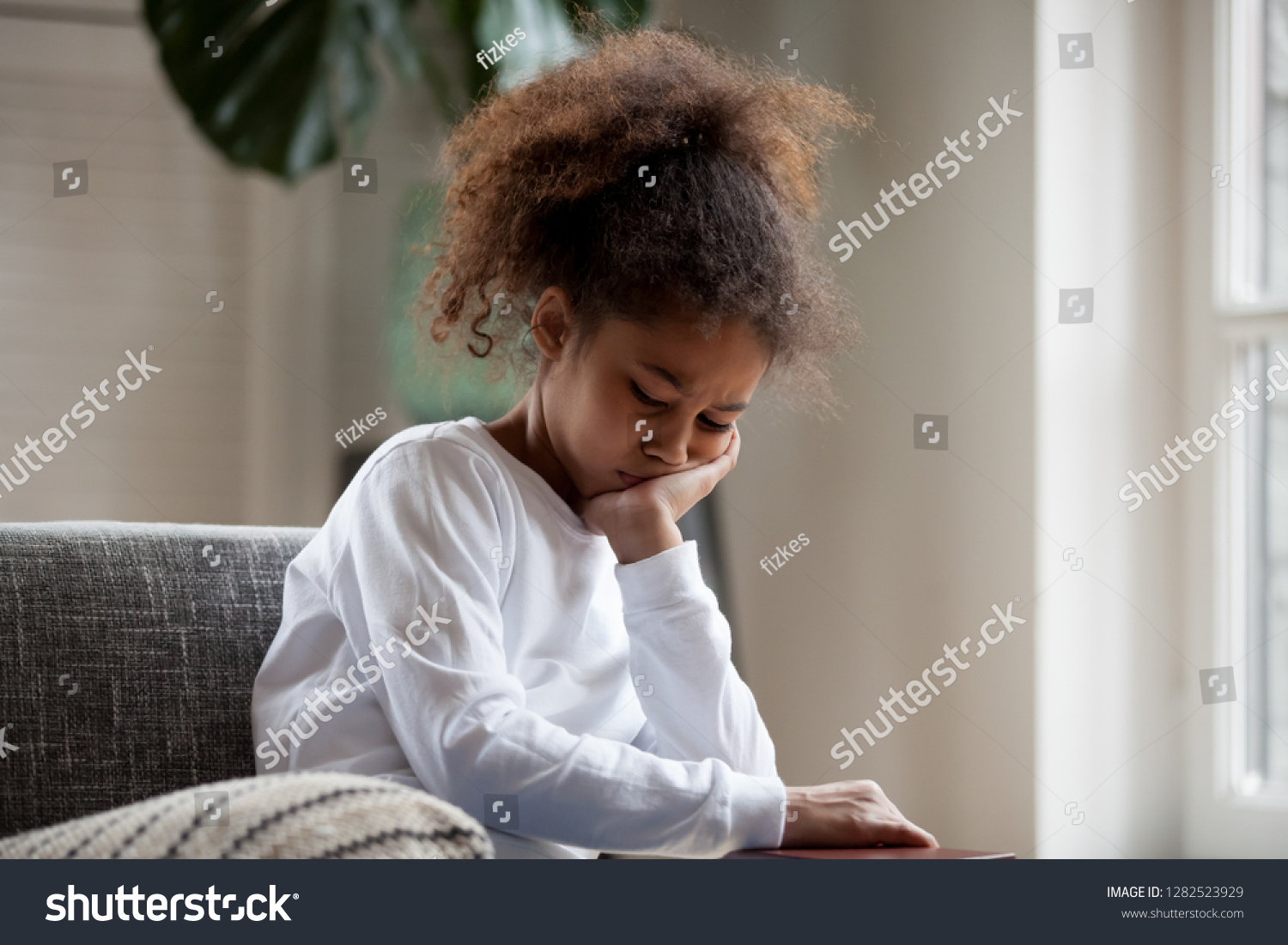 Upset little african american girl feels hurt sad bored sitting alone at home, depressed punished mixed race kid having psychological trauma, frustrated preschool black child thinking hiding problem #1282523929