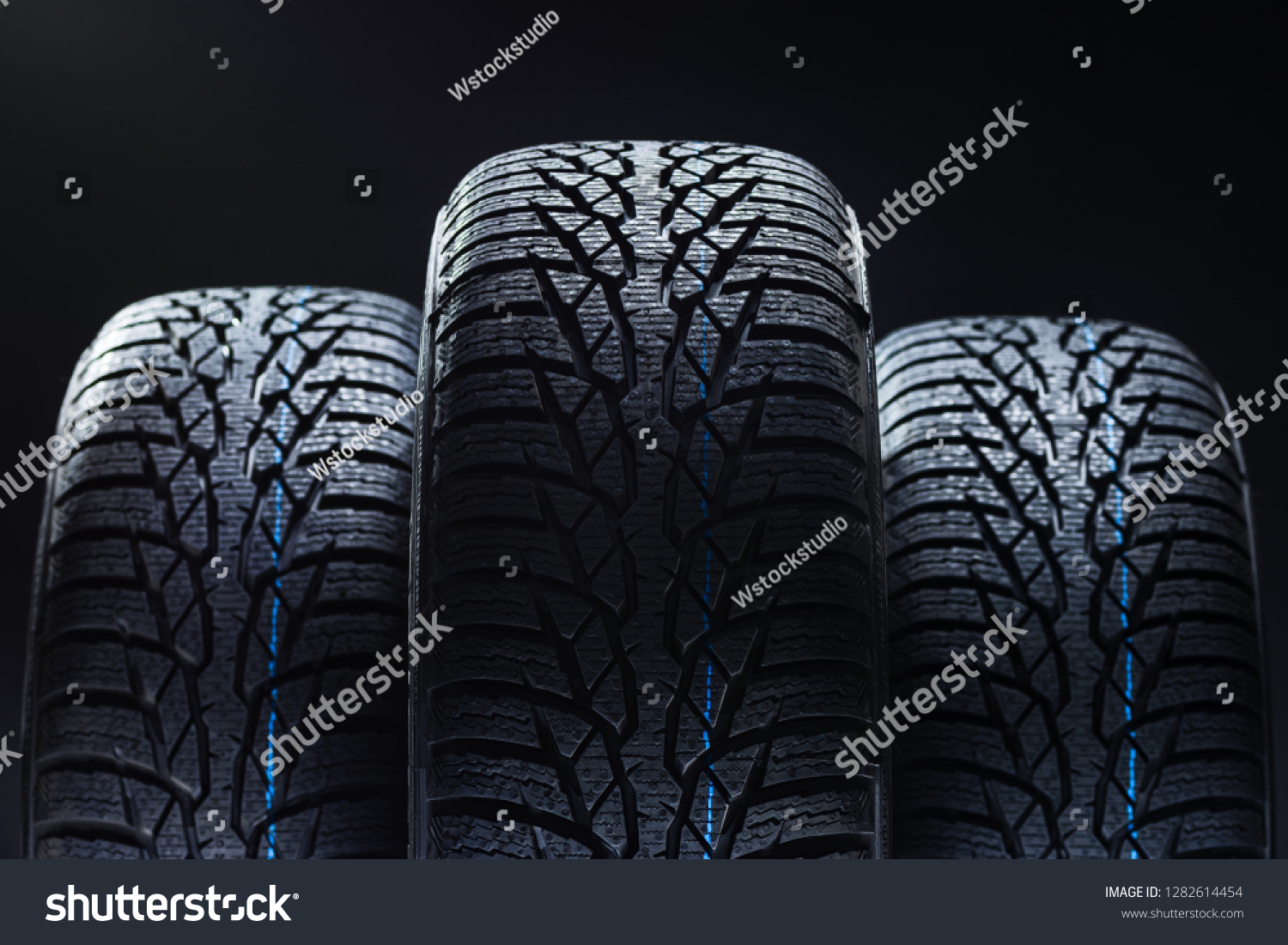 Set of new winter tires on black background with contrasty lighting. Close up product photograph of unused tyres #1282614454