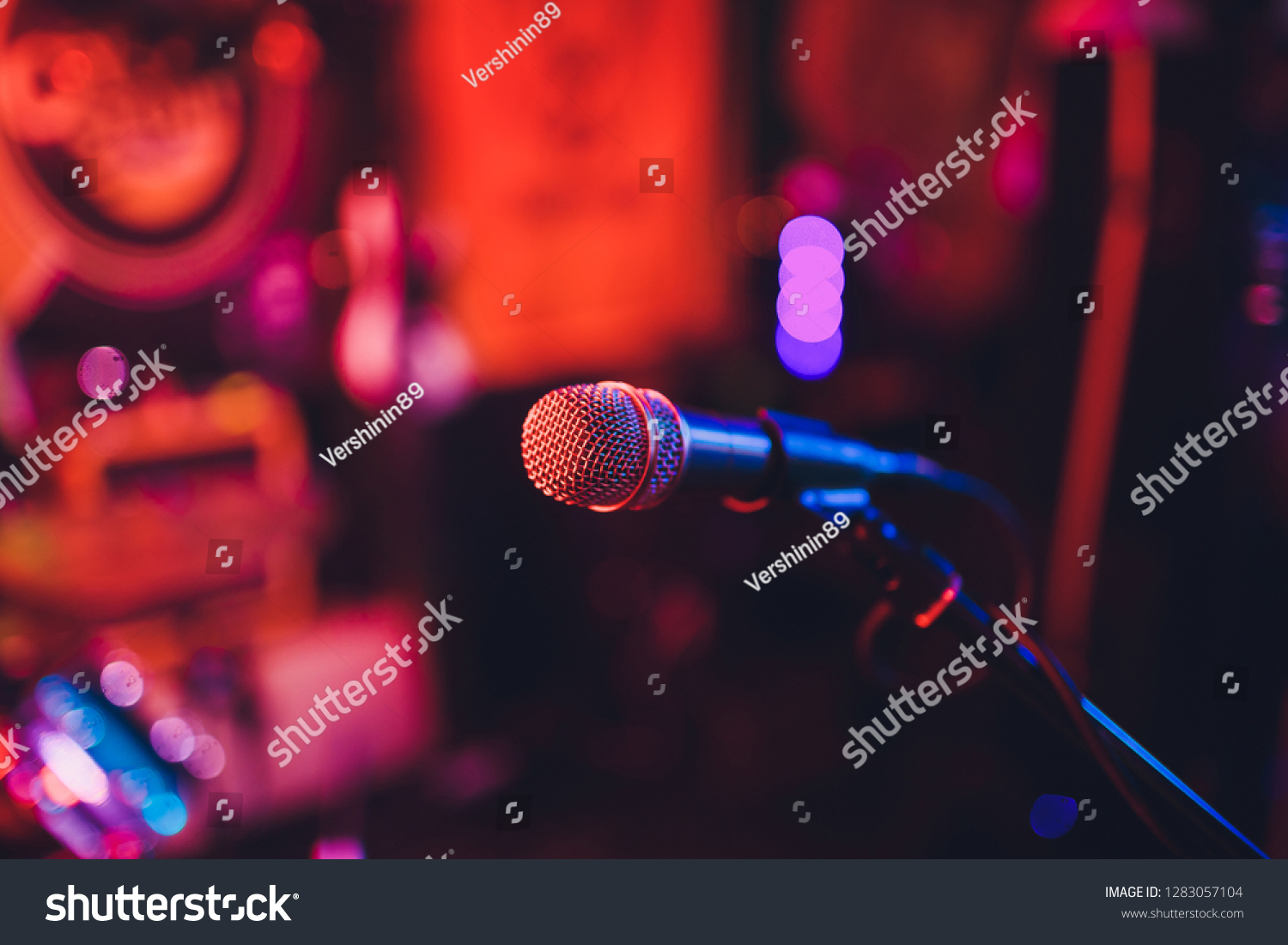 Microphone on a stand ready for live music performance or karaoke night with soft bokeh lights and people silhouettes in the background. Concept for musical singing event, having a good time. #1283057104
