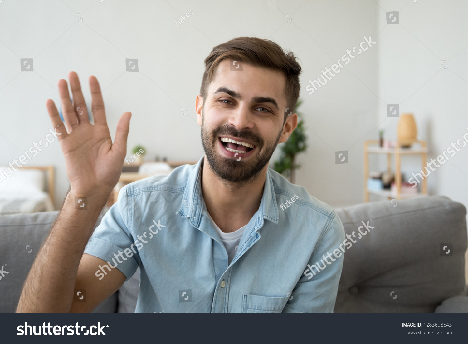 Friendly happy young man waving hand saying hello looking at camera greeting distant friend making online call, cheerful male vlogger blogger recording vlog teaching e-coaching via webcam, portrait #1283698543