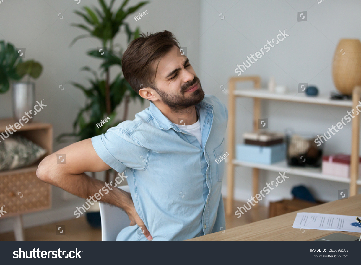 Tired exhausted man feeling pain in back suffering from lower lumbar backache herniated disc after sedentary work, fatigued man rubbing spine muscles sitting in incorrect posture, backpain concept #1283698582