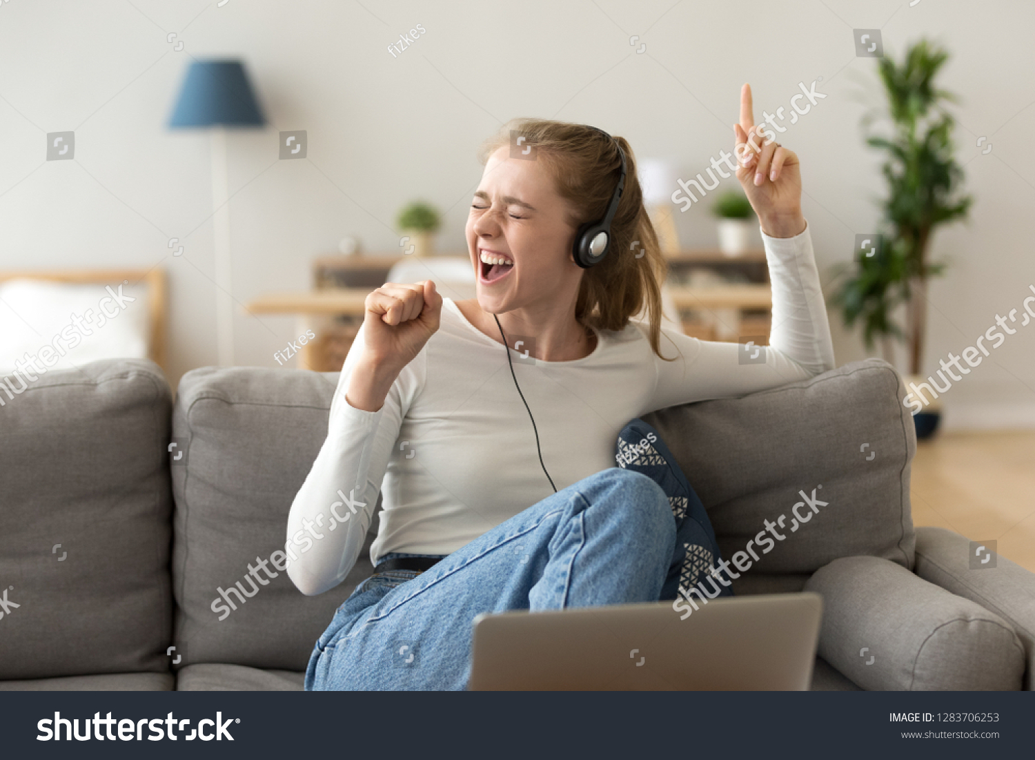 Funky teen girl singing favorite song listening to music podcast in headphones using app at home, happy funny young woman wearing headset enjoying new audio tracks playing in digital application #1283706253