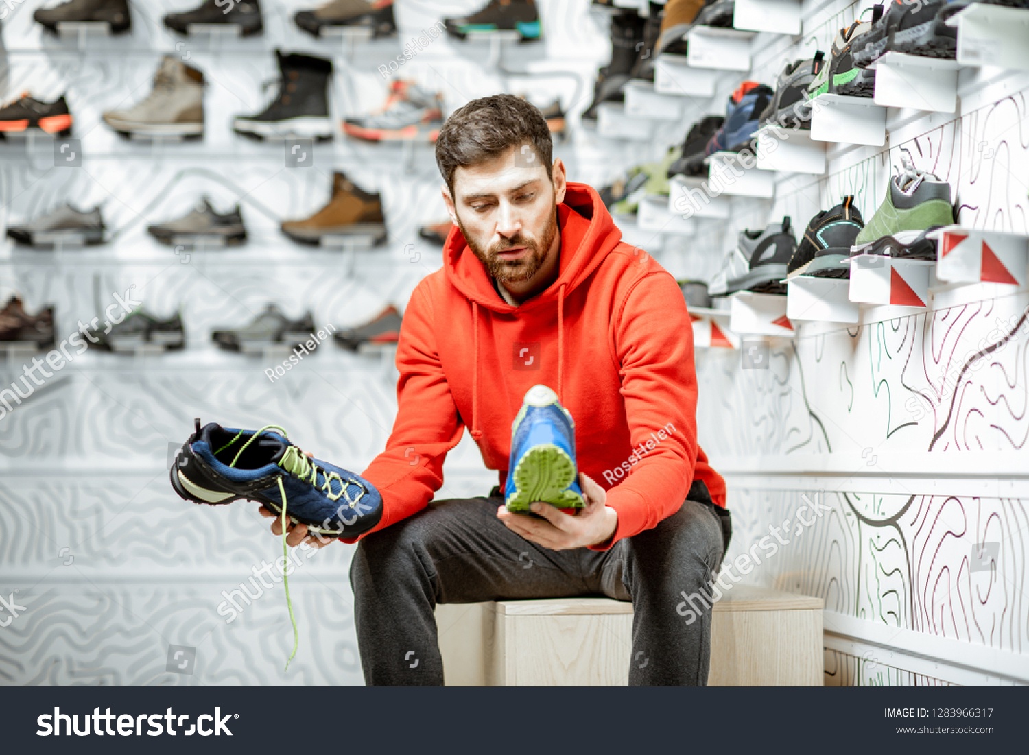 Man choosing trail shoes for hiking sitting in the fitting room of the modern sports shop #1283966317