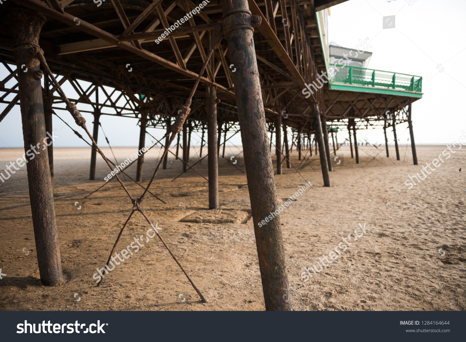 A beautiful old vintage steel iron victorian seaside pier structure shot from beneath, victorian architecture on the sandy beach, seaside landmark buildings. #1284164644