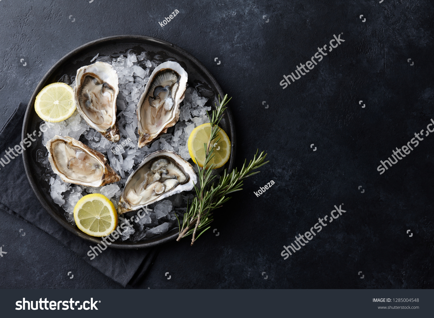 Fresh opened oysters in a plate with ice and lemon on black textured background, top view #1285004548