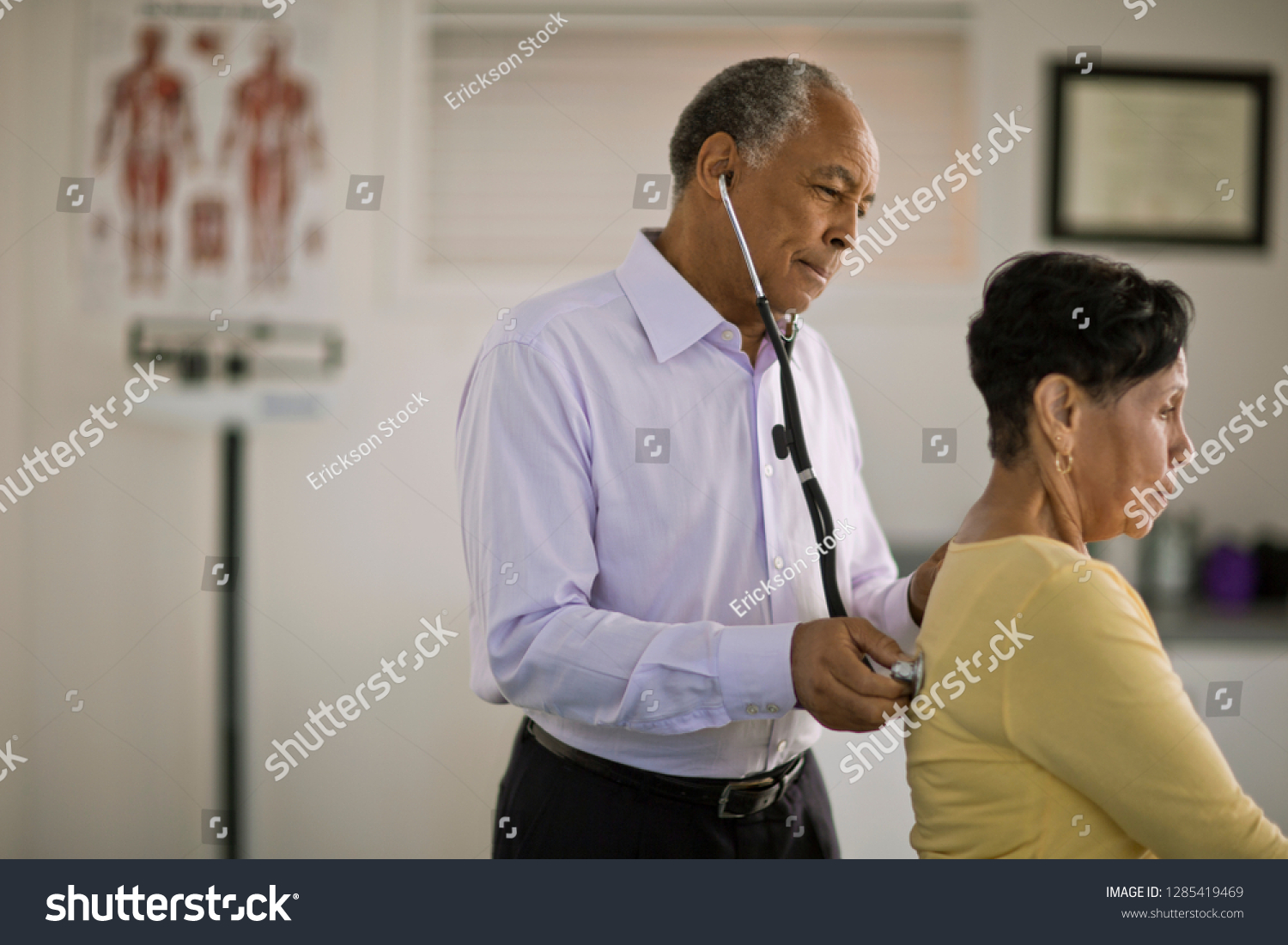 Male doctor listening to the heartbeat of a mature female patient inside his office. #1285419469