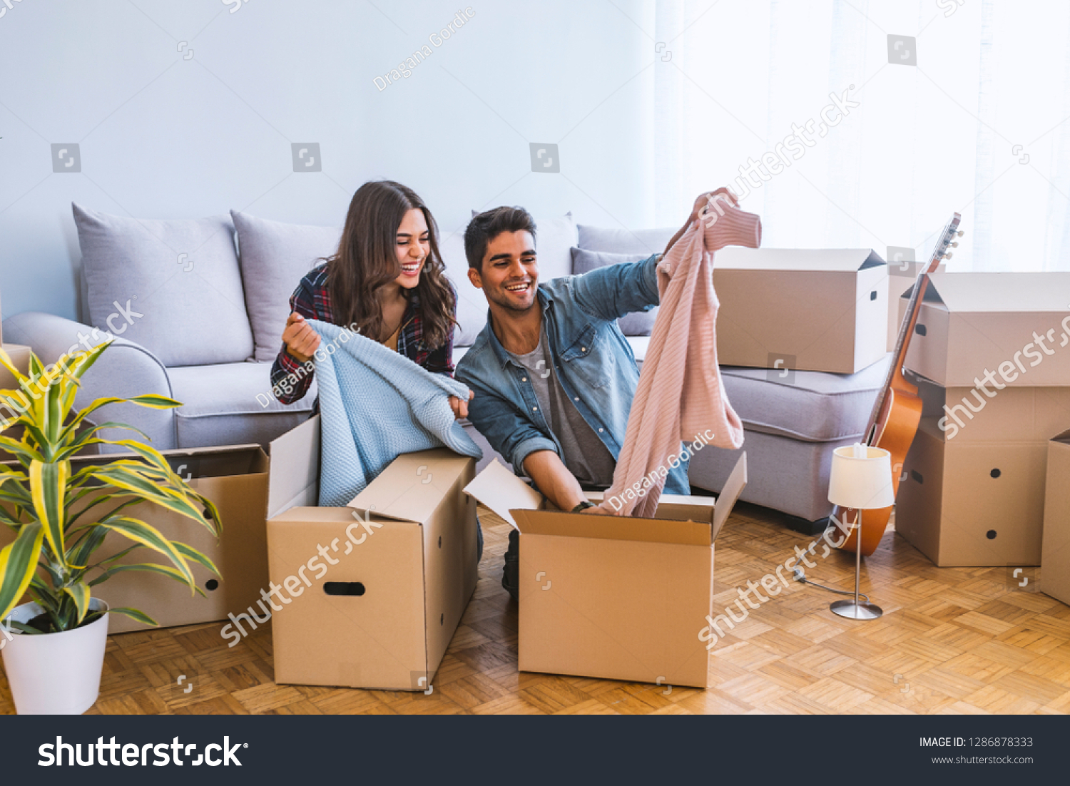 New Home. Funny young couple enjoy and celebrating moving to new home. Happy couple at empty room of new home. Happy couple is having fun with cardboard boxes in new house at moving day.  #1286878333