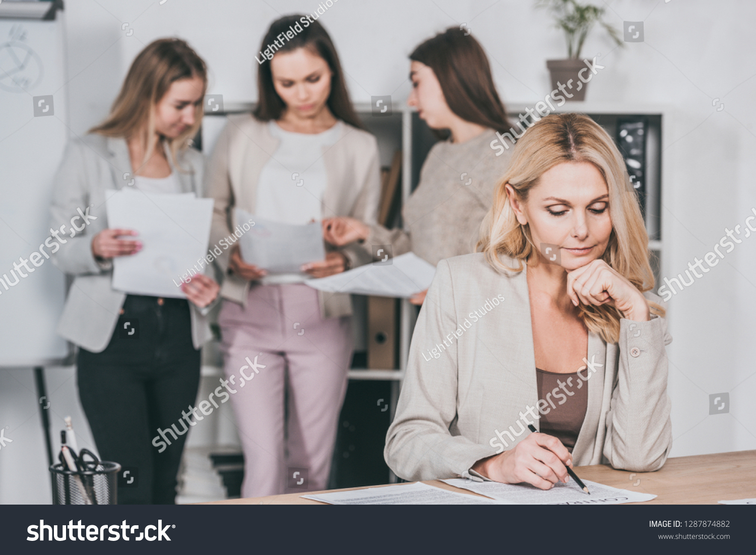 mature businesswoman working with contract and young businesswomen discussing papers behind in office #1287874882