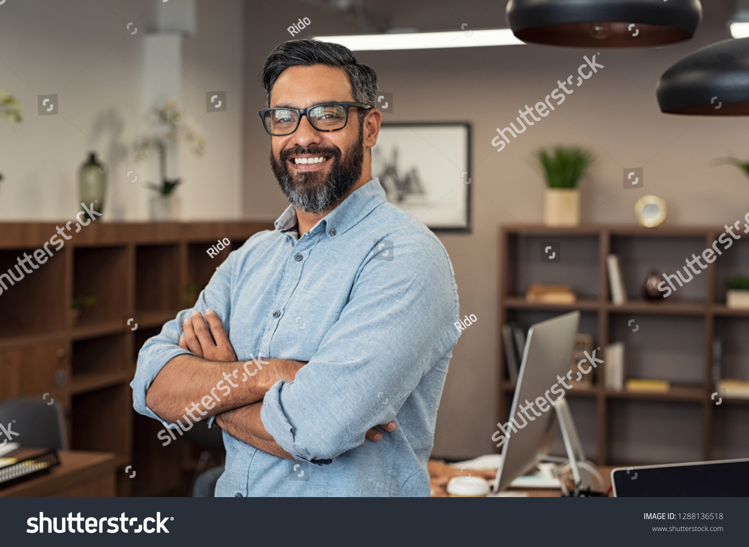 Portrait of happy mature businessman wearing spectacles and looking at camera. Multiethnic satisfied man  feeling confident in a creative office. Successful middle eastern business man smiling. #1288136518